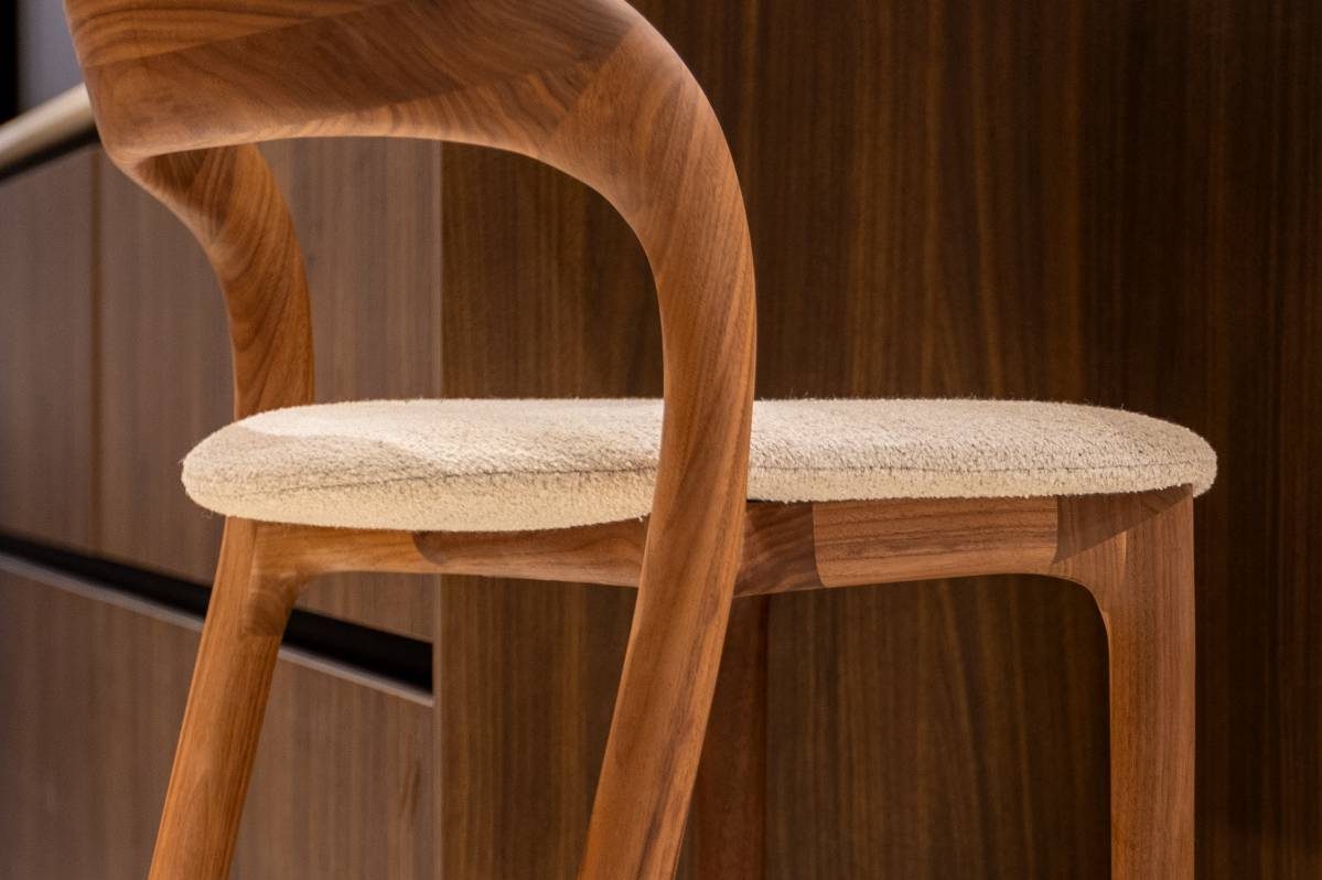 Close-up van barstoelen met notenhouten poten, aan een eiland met een notenhouten poot natuursteenlook werkblad met afgeronde hoeken.